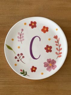 a plate with the letter c painted on it and flowers in the center, sitting on a wooden surface