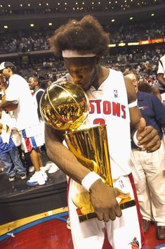 a basketball player holding a trophy in his right hand and looking down at the ground