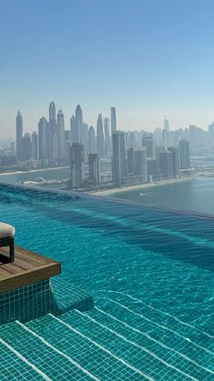 an outdoor swimming pool in front of a cityscape with the ocean and skyscrapers