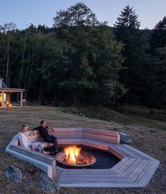 two people sitting around a fire pit in front of a house