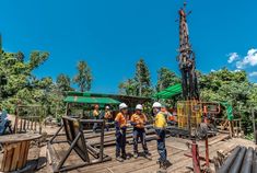 three men in hardhats and safety vests stand on a construction site next to an oil rig