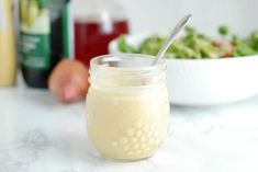 a glass jar with a spoon in it sitting on a table next to a bowl of salad