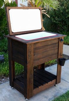 an outdoor cooler sitting on the side of a sidewalk next to some grass and bushes