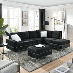 a living room with black couches and white pillows on the rugs in front of large windows