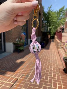 a person is holding up a pink keychain on a brick sidewalk with buildings in the background