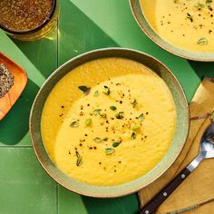 two bowls filled with soup sitting on top of a green table next to spoons