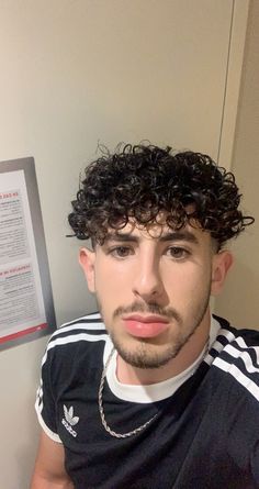 a man with curly hair wearing a black t - shirt and silver chain around his neck