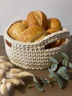 a basket filled with rolls next to a bunch of green leaves on top of a wooden table