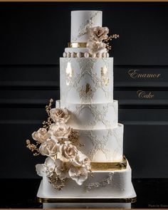 a three tiered white wedding cake with flowers on the side and gold trimmings