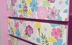 a pink and blue flowered wall hanging on the side of a purple cabinet in a bathroom