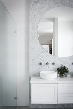 a white bathroom with a round mirror above the sink and a plant on the counter