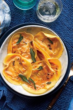 a bowl filled with ravioli on top of a blue cloth next to two glasses