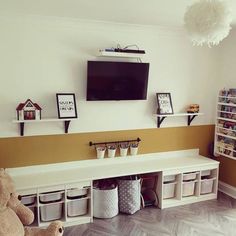 a tv mounted on the wall above a shelf filled with baskets and bins next to a teddy bear