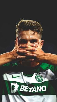 a man covering his face with his hands while wearing a green and white shirt in front of a black background