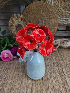 a blue vase filled with red flowers sitting on top of a woven table cloth next to wicker baskets