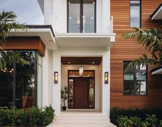 the front entrance to a modern home with wood and white trimmings, surrounded by greenery