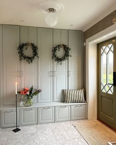 two wreaths hang on the wall next to a bench with flowers and candles in front of it