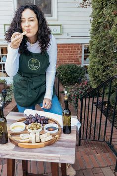 a woman sitting at a table with wine bottles and cheeses on it, making a funny face