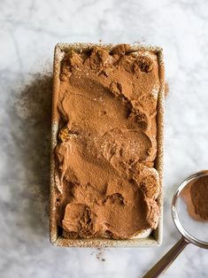 a pan filled with brownie batter next to a spoon on a white counter top