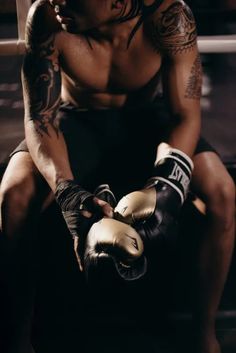 a man with tattoos sitting down wearing boxing gloves