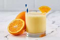 an orange smoothie with a blue and white striped straw next to two oranges