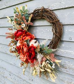 a wreath on the side of a building with flowers and leaves hanging from it's sides