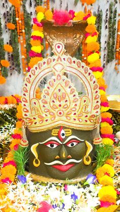 an elaborately decorated mask sits in front of flowers and garlands on the ground