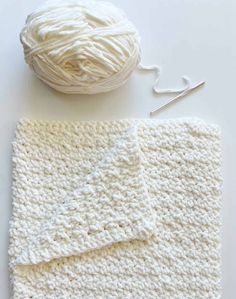 the crochet blanket is next to a ball of yarn and knitting needles on a white surface