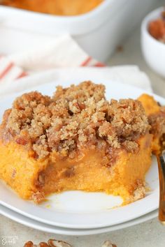 a white plate topped with a piece of cake next to a fork and bowl of nuts