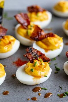 deviled eggs topped with bacon and chives on a baking sheet, ready to be eaten