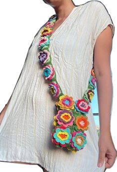 a woman wearing a white dress holding a multicolored crocheted flower necklace