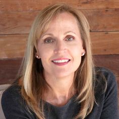 a woman with long blonde hair sitting in front of a wooden wall and looking at the camera