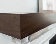 a close up view of a wood mantle in a living room with white walls and fireplace