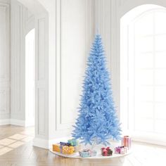 a blue christmas tree with presents under it in an empty room next to white walls