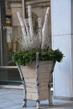 a wooden planter with branches and greenery in it on the side of a building