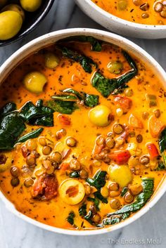 two bowls of soup with olives, spinach and other vegetables on the side