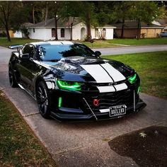 a black sports car with white stripes parked on the side of a road in front of a house