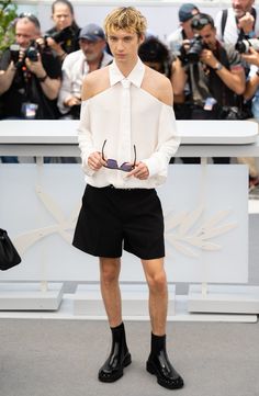 a man in black shorts and white shirt standing on the runway with cameras around him