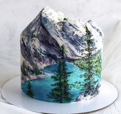 there is a cake decorated with mountains and trees on the top, along with blue water