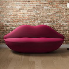 a red couch sitting in front of a brick wall with a lamp on top of it