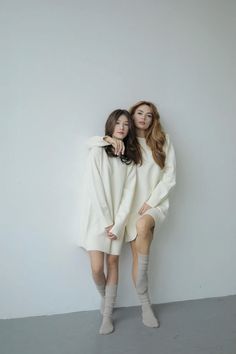 two women in white sweaters posing for the camera with their arms around each other