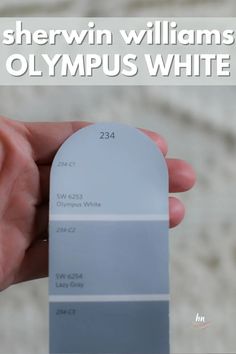 a person holding up a white and gray color swatch with the words sherwin williams olympic white on it