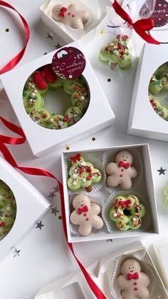 six decorated cookies in white boxes with red ribbon around them on top of a table