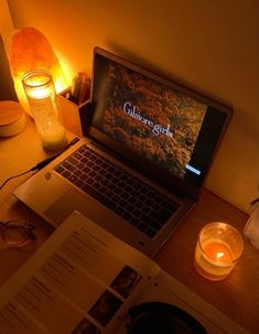 an open laptop computer sitting on top of a desk next to a candle and book