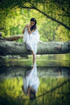 a woman is standing on a log in the water with her hands behind her back