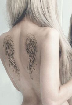 the back of a woman's body with angel wings tattooed on her upper half