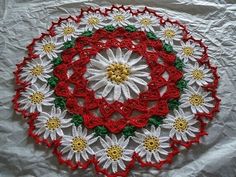 a crocheted doily with red, yellow and green flowers on it sitting on a white sheet