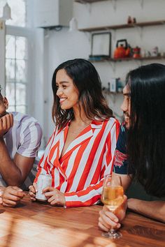 three people sitting at a table talking to each other and drinking wine in front of them