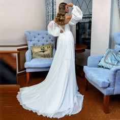 a woman in a white dress is standing near a blue chair and looking into the mirror