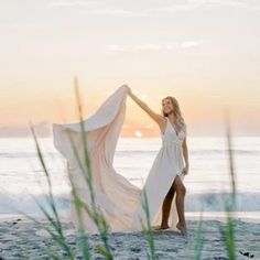 a woman standing on top of a beach next to the ocean holding a white dress